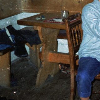 Two people sitting indoors, smiling in a rustic kitchen.