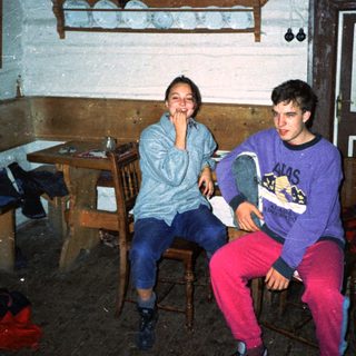 Two people sitting indoors, smiling in a rustic kitchen.