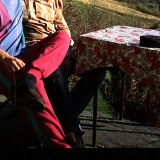 Two people sitting outdoors on chairs, enjoying scenic countryside view.