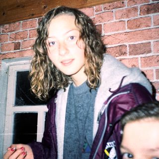 Young woman standing near brick wall doorway.