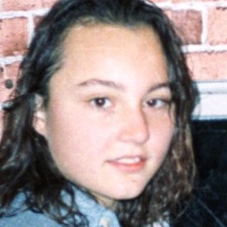 Young woman standing by brick wall near open window.