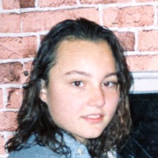 Young woman standing by brick wall near open window.