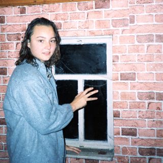 Young woman standing by brick wall near open window.