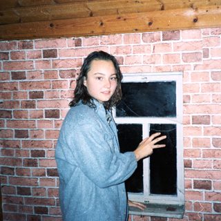 Young woman standing by brick wall near open window.