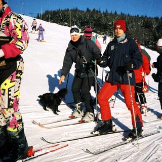 People skiing on snow with a dog.