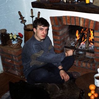 Cozy room with man sitting by lit fireplace.
