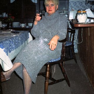 Woman in cozy sweater holding wine glass indoors.