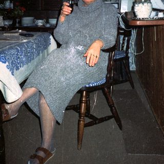 Woman in cozy sweater holding wine glass indoors.