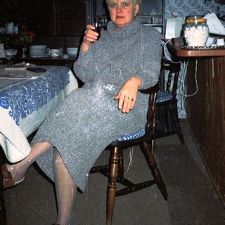 Woman in cozy sweater holding wine glass indoors.