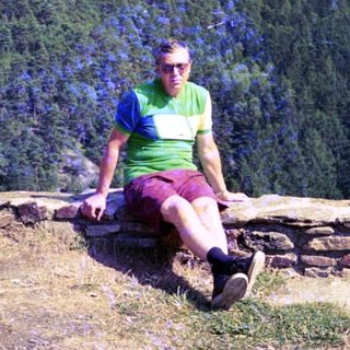 Person sitting on stone wall in forested hillside.