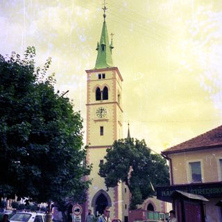 Historic town square with church tower, people walking, vintage cars.