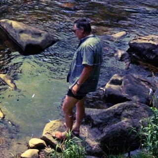 Family enjoying shallow river water near rocks.