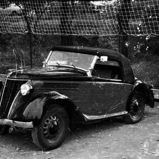 Vintage car damaged near tennis court.