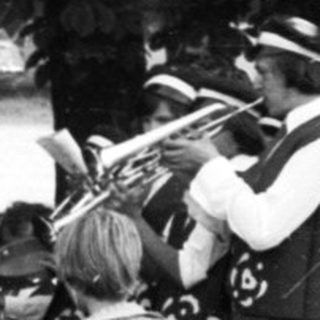 Funeral procession with brass band playing at gravesite.