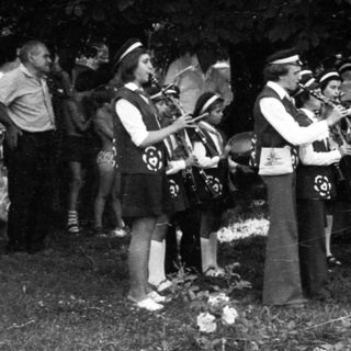 Funeral procession with brass band playing at gravesite.