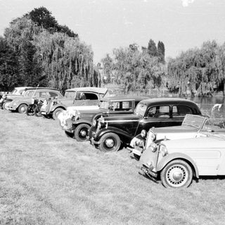 Vintage cars parked by a lake.