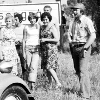 Group posing with vintage truck near roadside sign.
