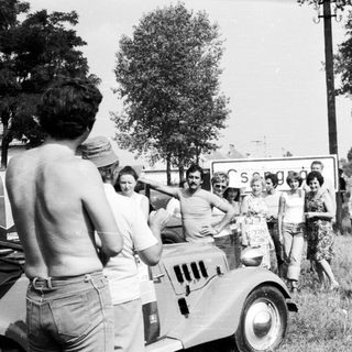 Group posing with vintage truck near roadside sign.