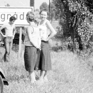 Vintage rally car with participants near roadside sign.