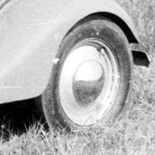 Vintage rally car with participants near roadside sign.