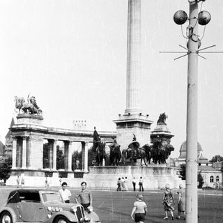 Historic monument with statues, vintage car, pedestrians.