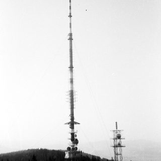 Tall communication tower with aircraft on hilltop.