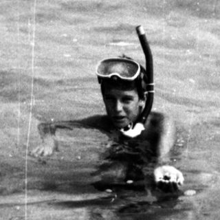 Child snorkeling in crowded shallow ocean waters.