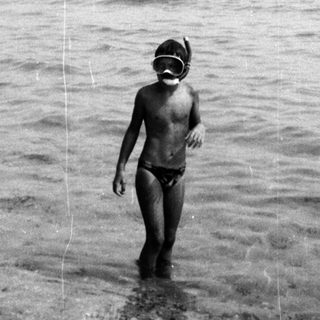 Child in snorkel gear entering shallow ocean.