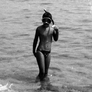 Person in swim cap wading into crowded ocean.