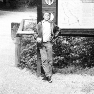 Man posing near "Boubinský Prašivý" sign in forest.