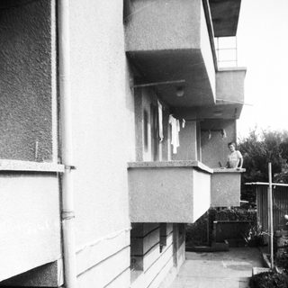 Residents on apartment balconies in narrow outdoor corridor.