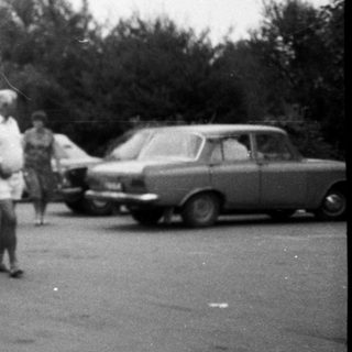 Vintage bus pulling small trailer with people outside.