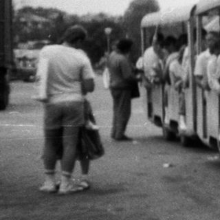 Vintage bus pulling small trailer with people outside.