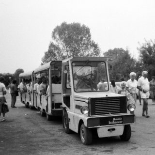 Vintage bus pulling small trailer with people outside.