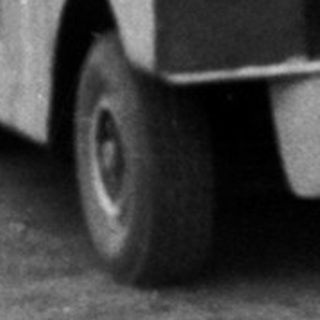 Vintage bus pulling small trailer with people outside.