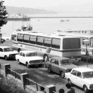 Bus terminal by coastal roadside with parked buses.