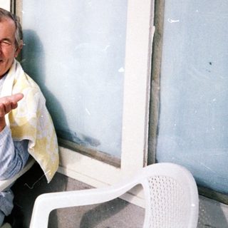 Man sitting indoors by open door, waving.