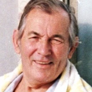 Man sitting indoors by open door, waving.