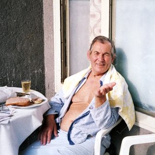 Man sitting indoors by open door, waving.
