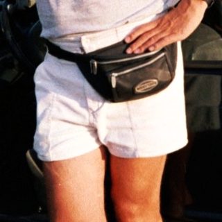Person standing by open car door wearing shorts, sunglasses, and fanny pack.