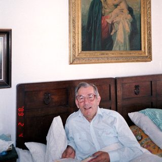 Man sitting on bed with religious painting above him.