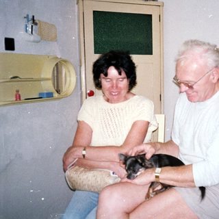Two people holding and smiling with small dog.