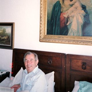 Man smiling in room with religious painting above wooden dresser.