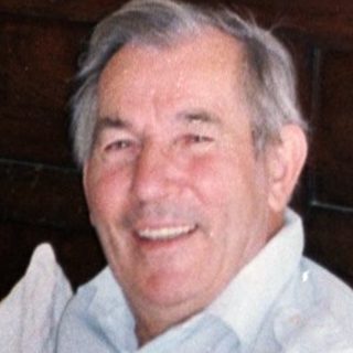 Man smiling in room with religious painting above wooden dresser.