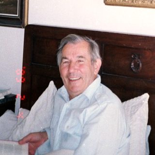 Man smiling in room with religious painting above wooden dresser.