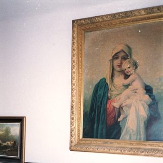 Man smiling in room with religious painting above wooden dresser.
