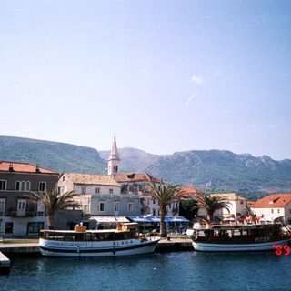 Mediterranean coastal town with boats, historic buildings, and mountains.