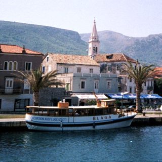 Mediterranean coastal town with boats, historic buildings, and mountains.