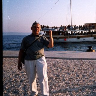 Man poses by pebble shore near crowded ferry boat.