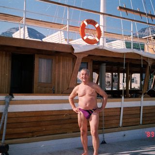Shirtless man in swim trunks posing near lifebuoy on boat.